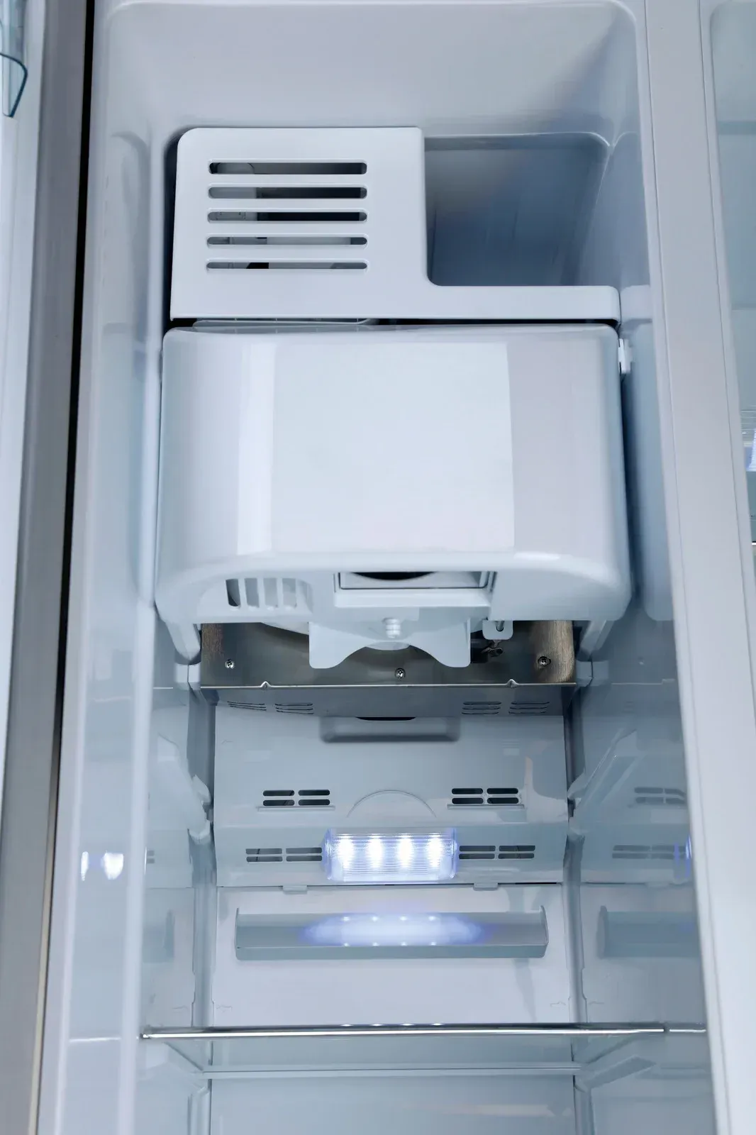 Inside a refrigerator: ice maker and storage bin, with internal lighting.