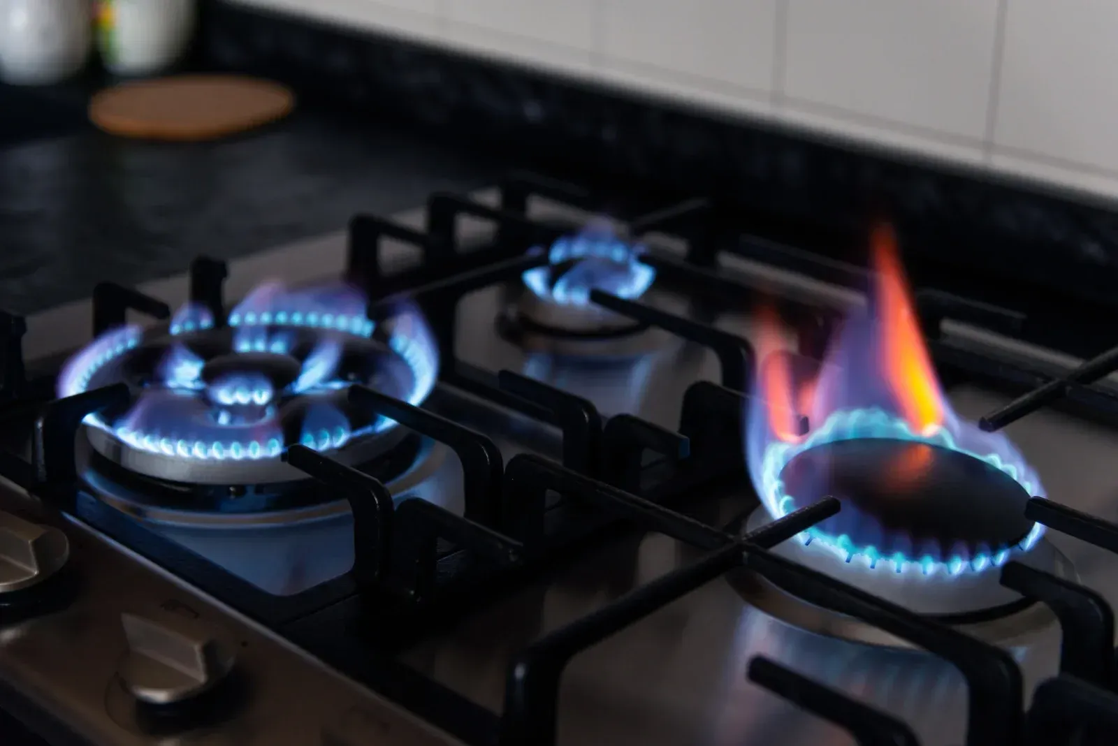 Gas stove burners with blue and orange flames lit on a black surface.