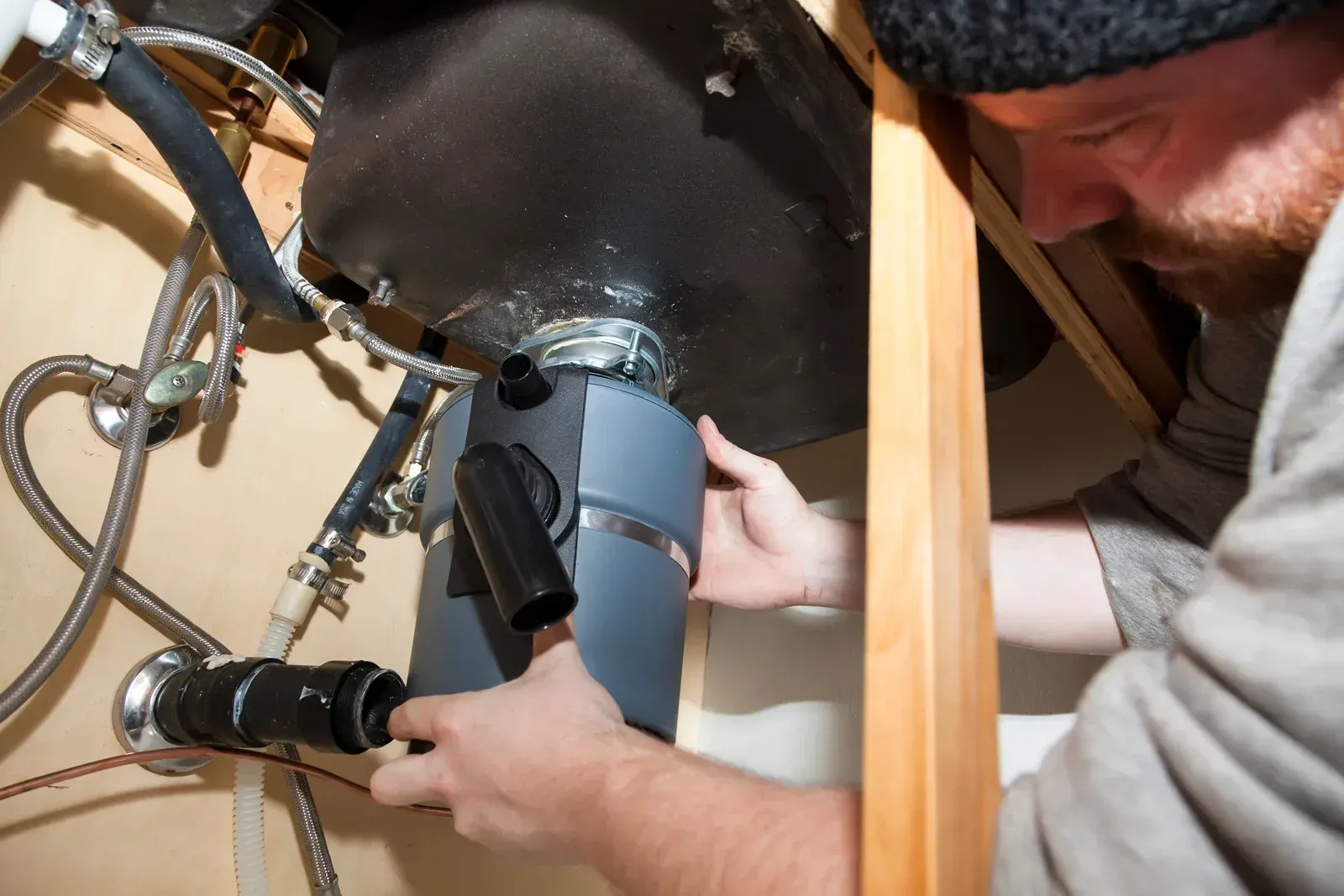 Person installing a garbage disposal under a kitchen sink.