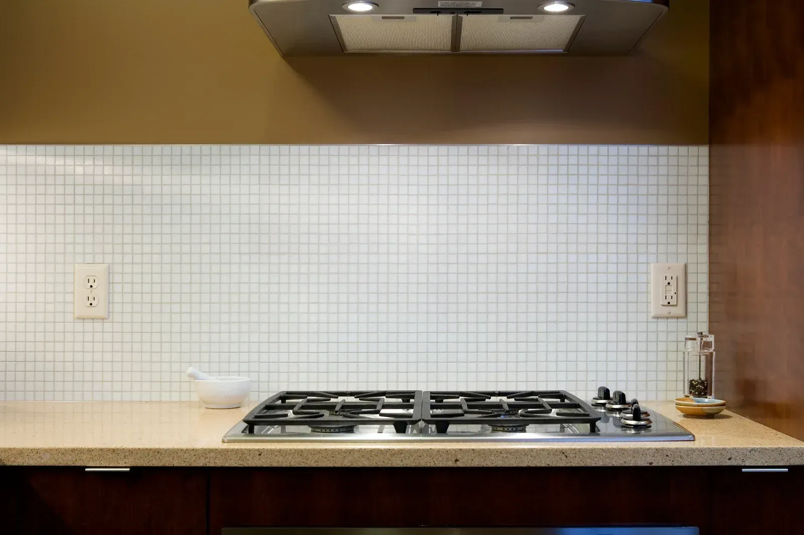 Kitchen with gas stovetop, white tiled backsplash, and range hood.