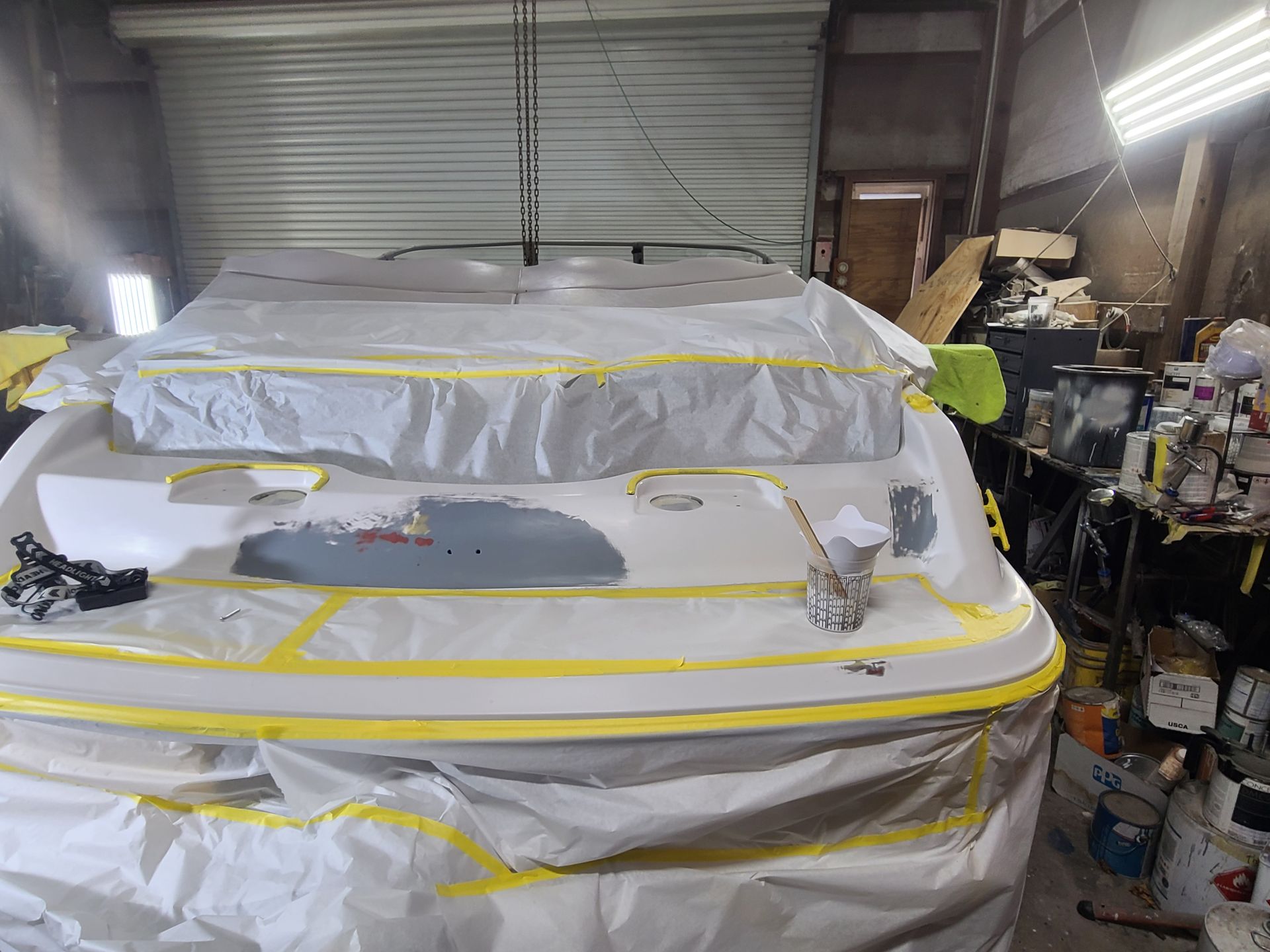 A boat being prepped for painting in a workshop, with masked-off surfaces and exposed filler areas on the deck.