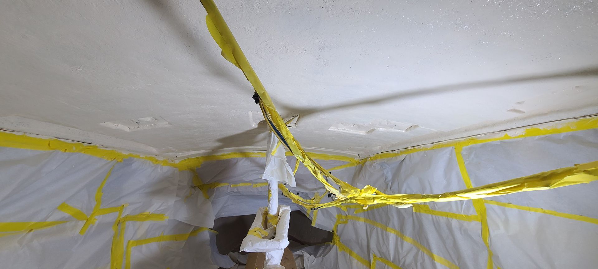 A white ceiling covered in plastic sheeting, secured with yellow tape, indicating an area under construction or repair.