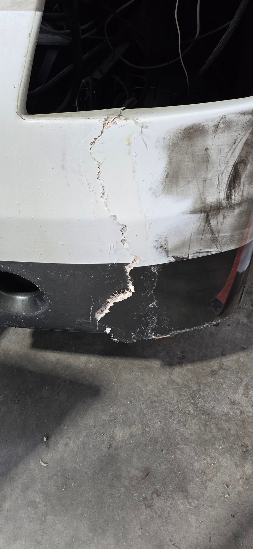 A close-up view of a vehicle bumper showing a significant vertical crack spanning both the white and black sections.
