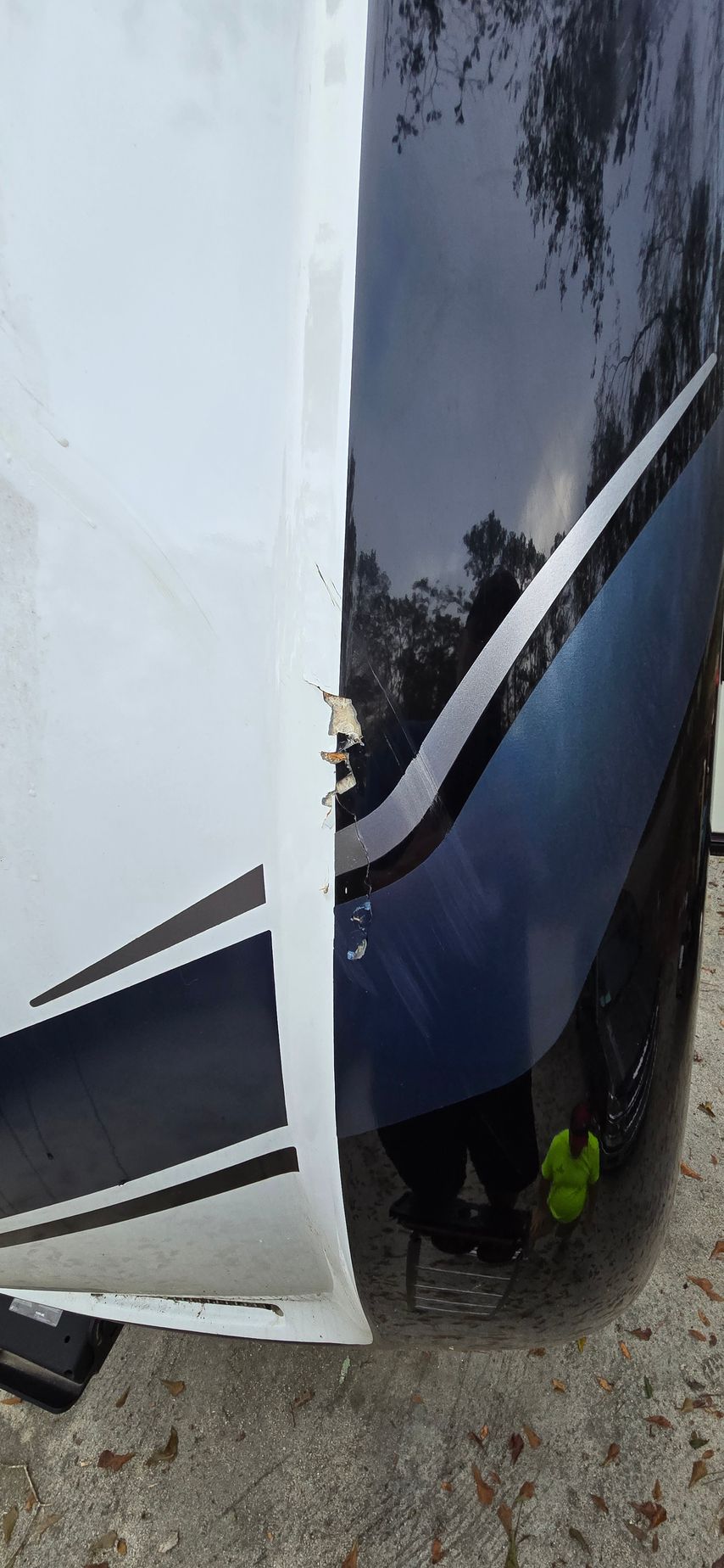 A close-up view of a vehicle's side panel showing chipped white paint and dark blue trim against a reflective surface.