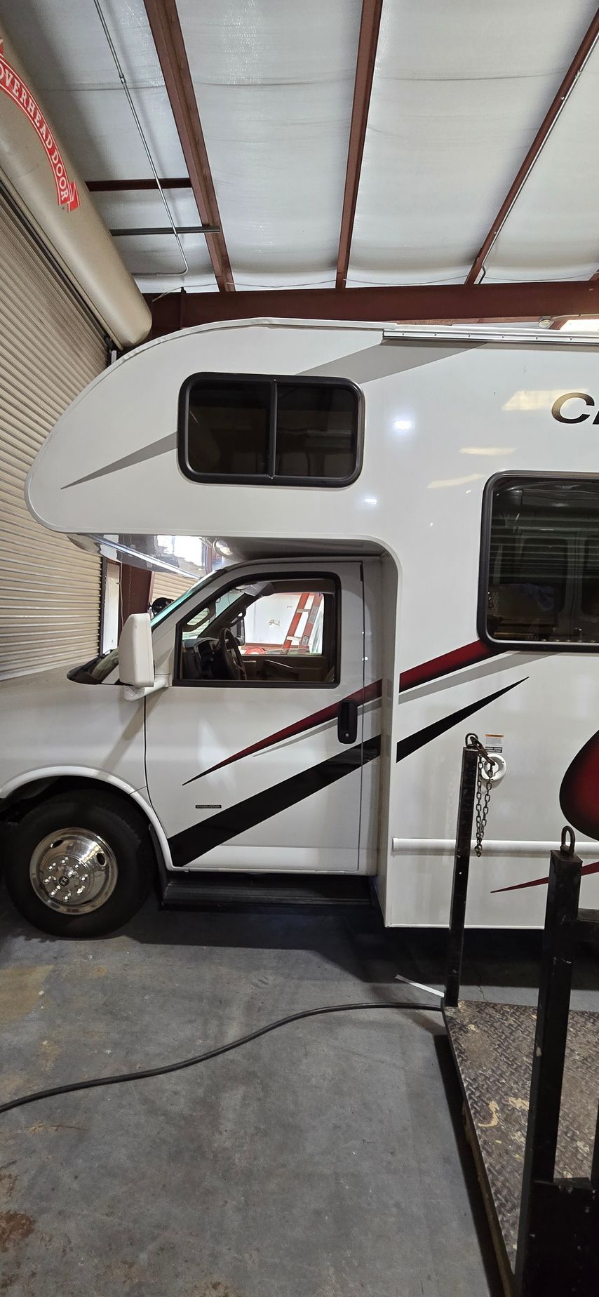 A side view of a white Class C motorhome parked inside an industrial building with a metal wall and ceiling.