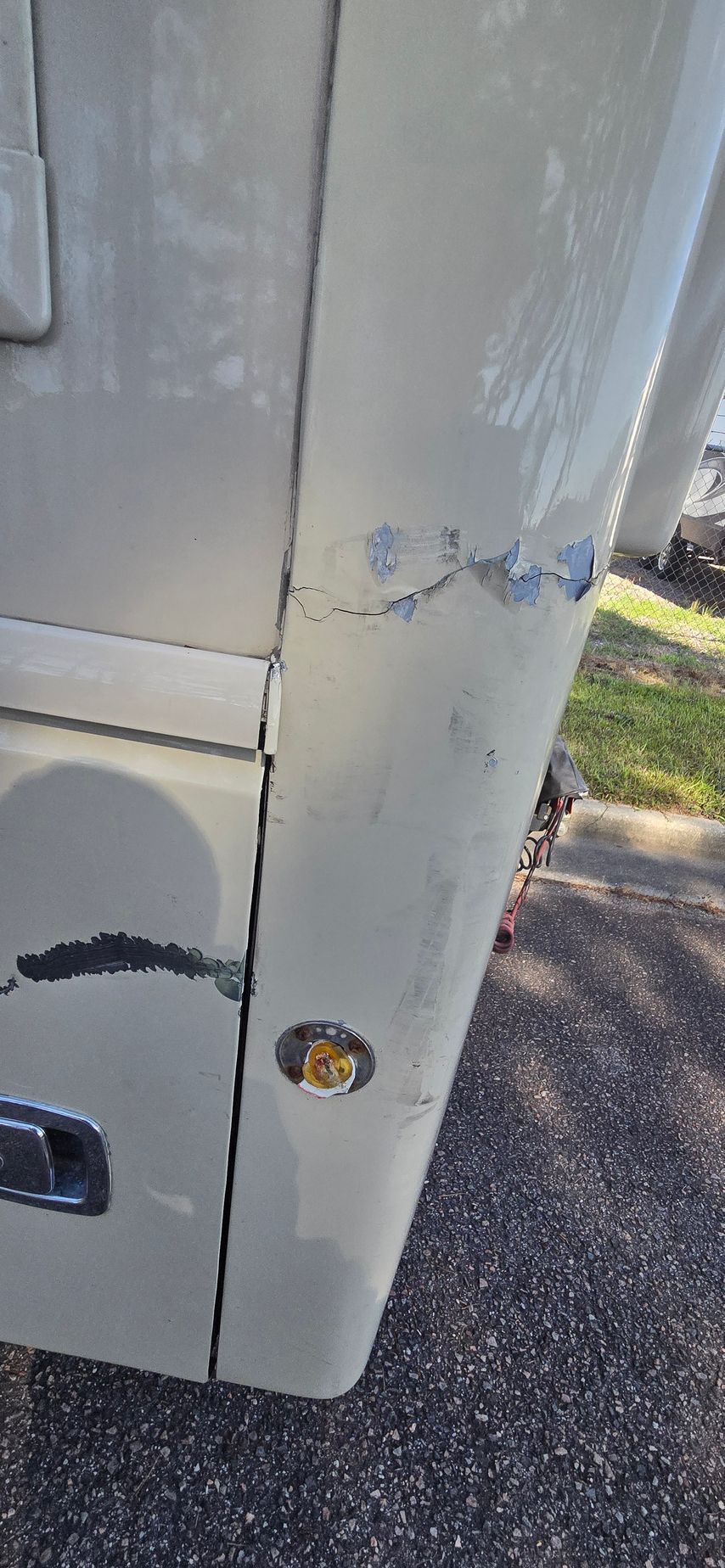 A close-up view of a white vehicle panel showing peeling paint, cracking, and surface damage near a small amber light.