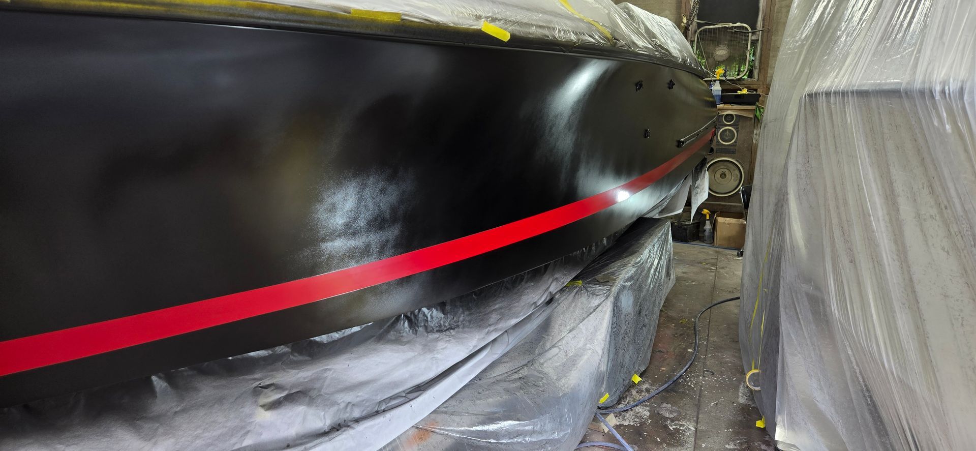 A freshly painted black boat hull with a bright red stripe running along the side, inside a workshop.