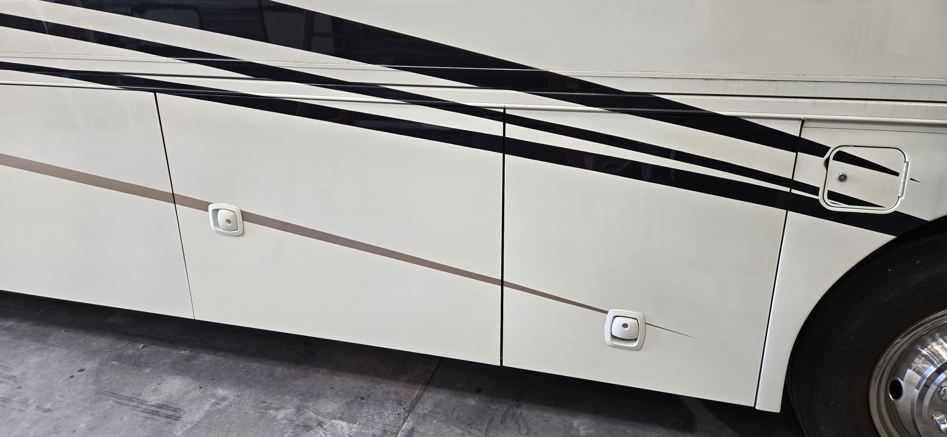 A close-up view of a cream-colored RV side panel featuring horizontal black stripes and two lockable storage compartments.