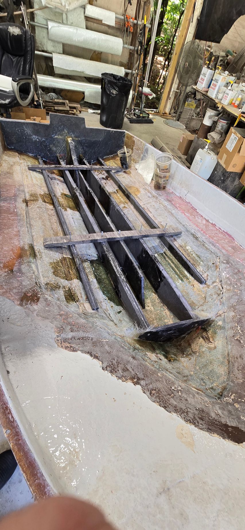 A boat hull interior showing a structural fiberglass stringer system under construction within a workshop.