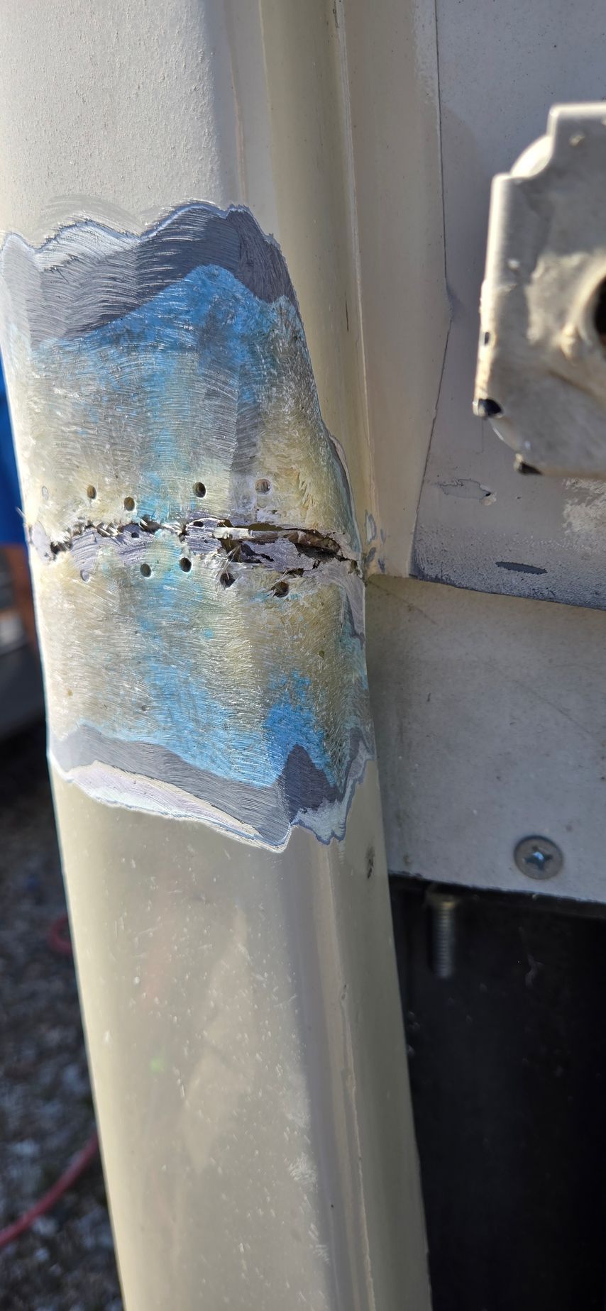 A vertical metal pole with a patch of chipped, peeling paint revealing layers of grey, blue, and yellow beneath.