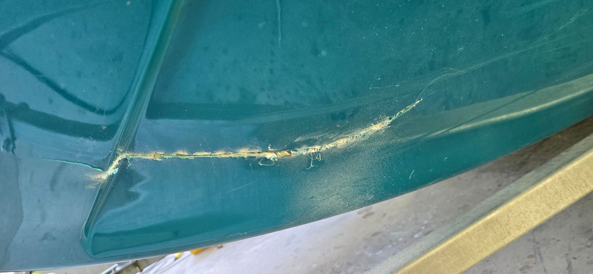 A close-up of a deep, yellowish crack in the teal, glossy exterior surface of a vehicle or boat.