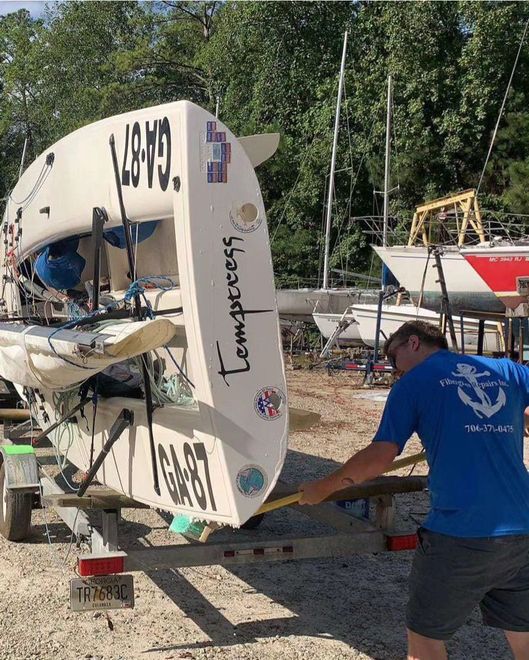 A person in a blue t-shirt measures a sailboat named