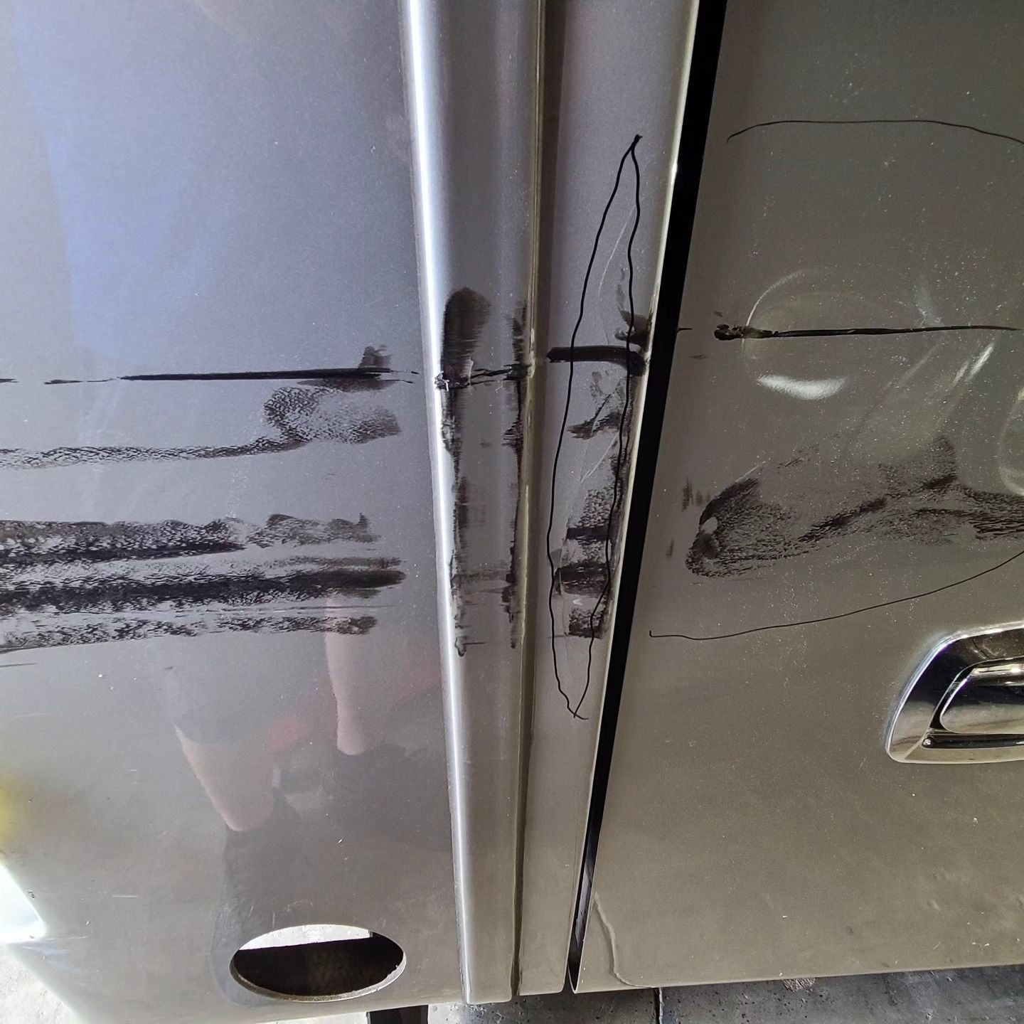 A close-up of a vehicle's side panels showing heavy black scuffs and deep scratches near the door seam and handle.