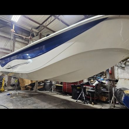 A sleek, white and blue boat hull suspended in the air inside a workshop or garage environment.