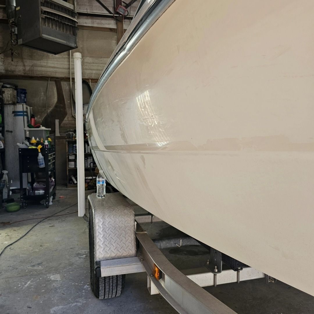 A close-up view of the side of a cream-colored boat hull resting on a metal trailer inside a workshop.