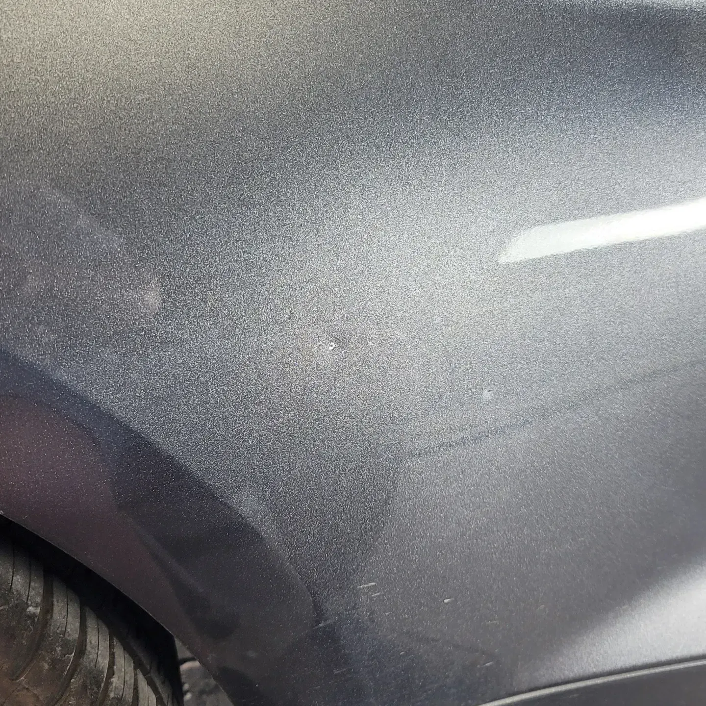 A close-up view of the metallic dark gray body panel of a car, showing paint texture and a light reflection.