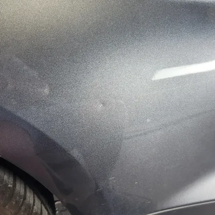 A close-up view of the metallic dark gray body panel of a car, showing paint texture and a light reflection.