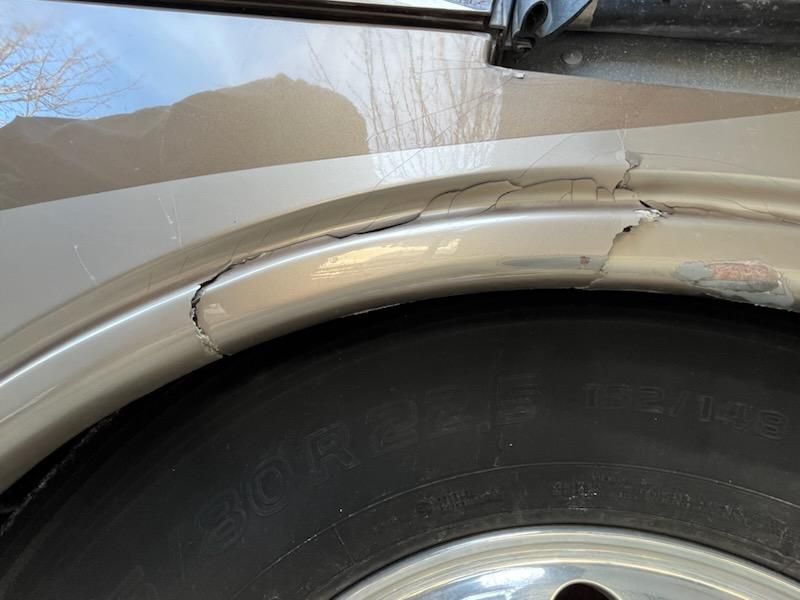 A close-up of a damaged, cracked tan fender flare above a vehicle tire.