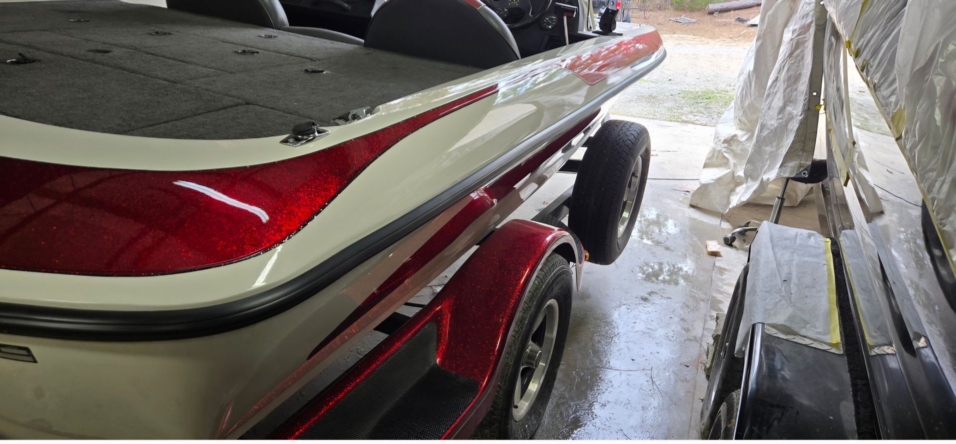 A close-up view of a red and white bass boat parked on a trailer inside a garage.
