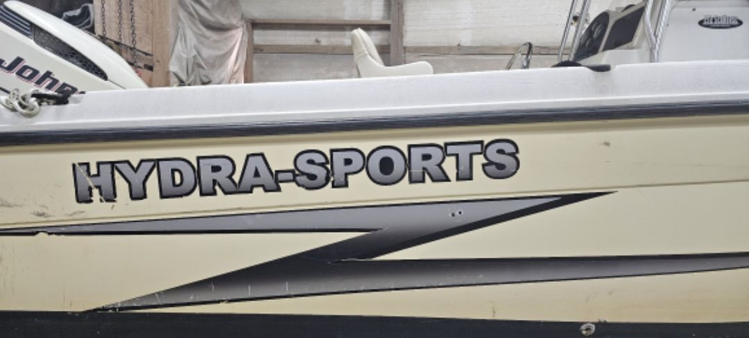 The side of a cream-colored Hydra-Sports boat featuring a large black lightning-bolt-shaped decal and outboard motor.