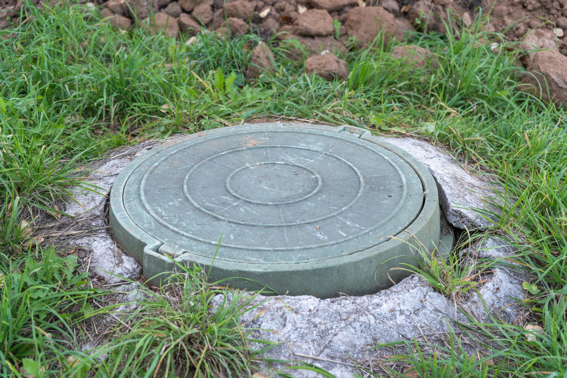A green manhole cover is sitting in the middle of a grassy field.