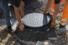 Two men are working on a manhole cover on the ground.