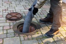 A man is pumping water into a manhole cover with a vacuum hose.