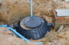 A septic tank is sitting in the dirt next to a brick wall.