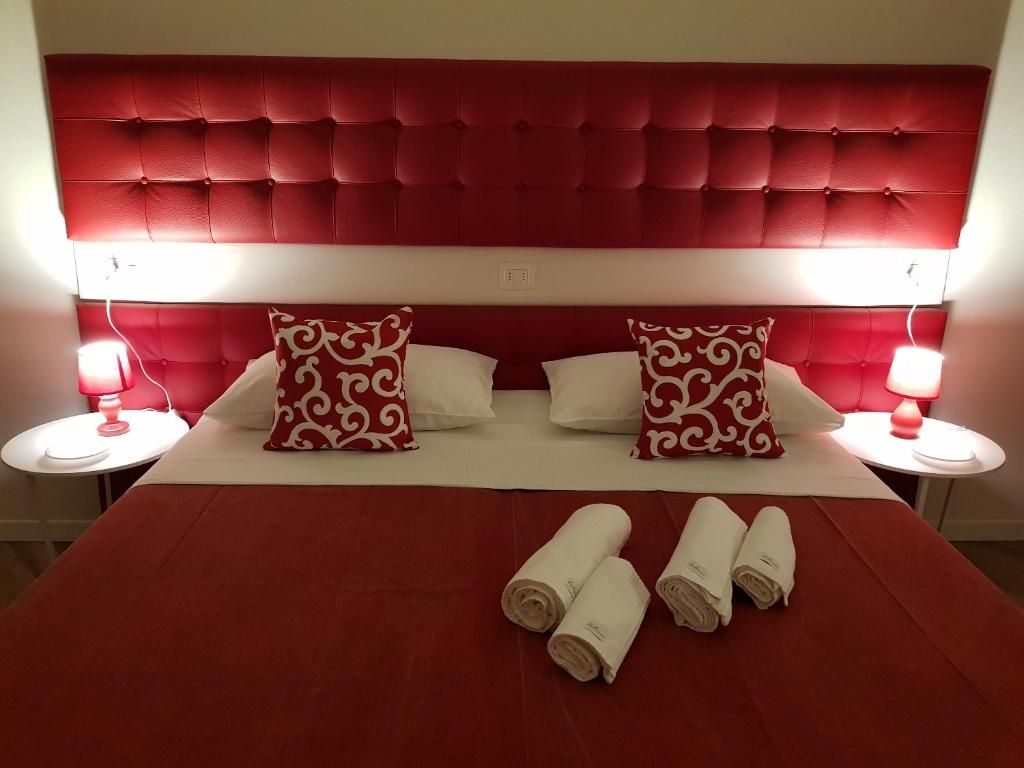 Camera da letto sui toni del rosso con letto grande, testiera rossa, biancheria bianca, cuscini decorativi e lampade da comodino.