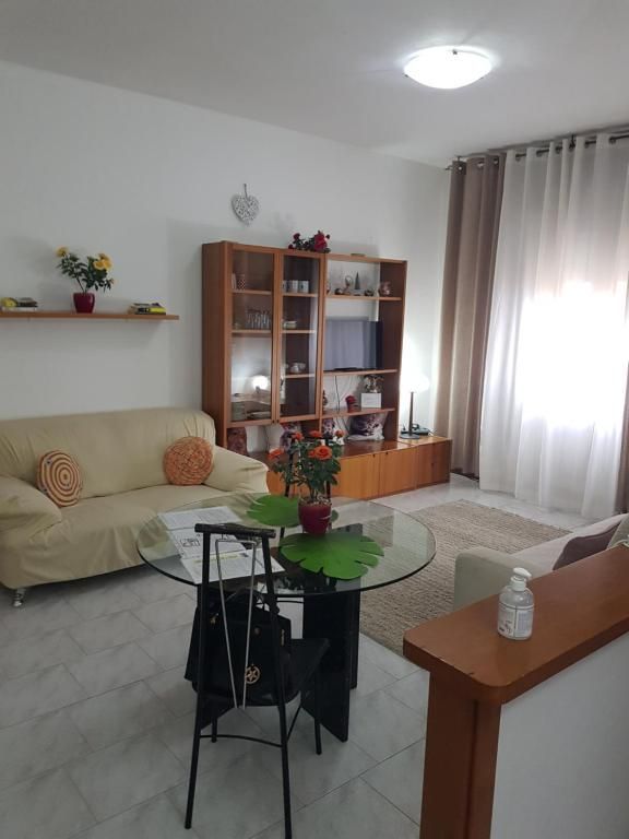 Soggiorno con divano, TV, tavolo rotondo e mobile in legno. Pareti bianche e pavimento piastrellato.