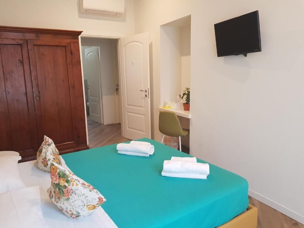 Camera da letto con letto turchese, armadio in legno e una piccola scrivania; pareti bianche e TV.