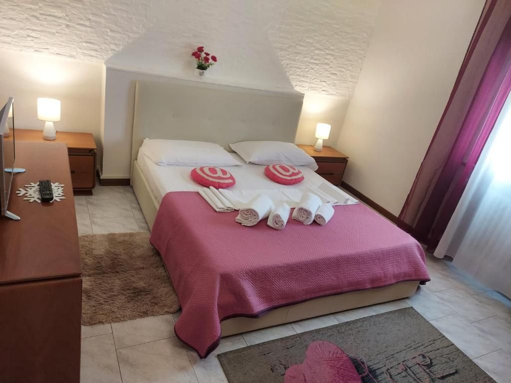 Camera da letto con letto matrimoniale, biancheria rosa, comodini, lampade e TV.