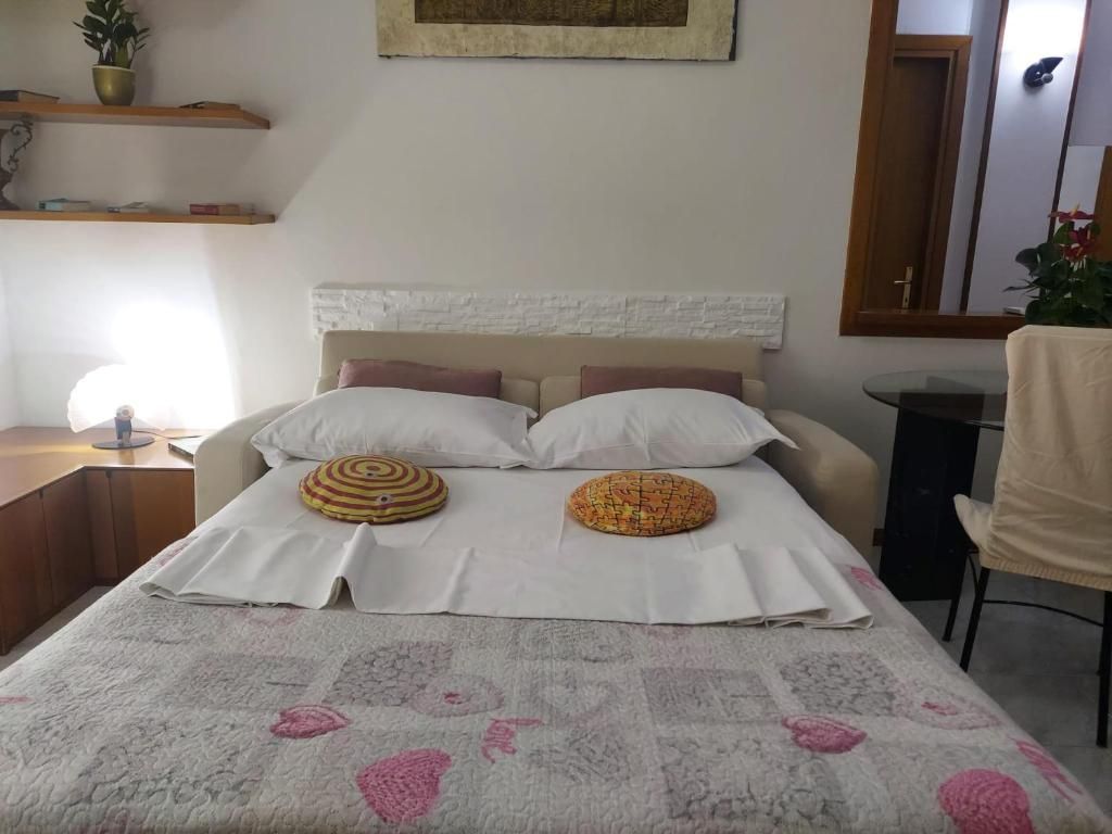 Camera da letto con letto matrimoniale, due cuscini rotondi decorativi, scrivania, sedia e specchio a parete.