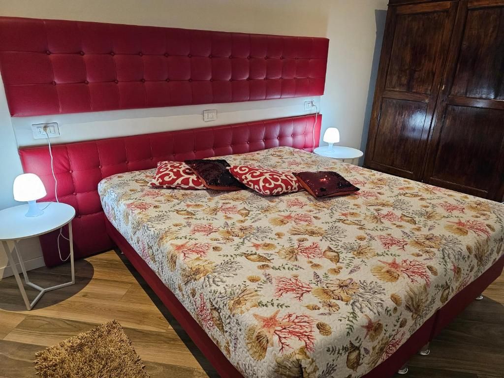 Letto imbottito rosso in una camera da letto con biancheria floreale, comodini e armadio in legno.