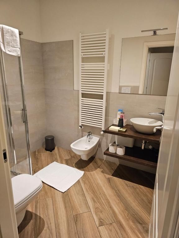 Bagno moderno con doccia, bidet, lavandino e scaldasalviette. Pavimenti in legno chiaro e pareti piastrellate grigie.