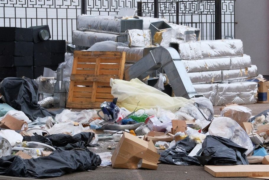 Overflowing trash and recycling bags piled in a street near stacked pallets and bundled materials.