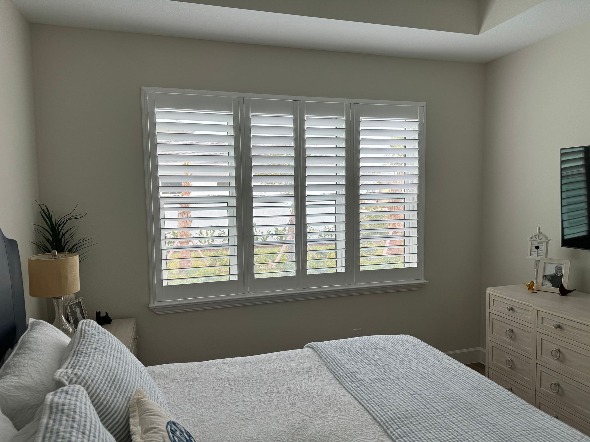 A bedroom with a bed, dresser and window with shutters — Deland, FL — Island Shutter Company