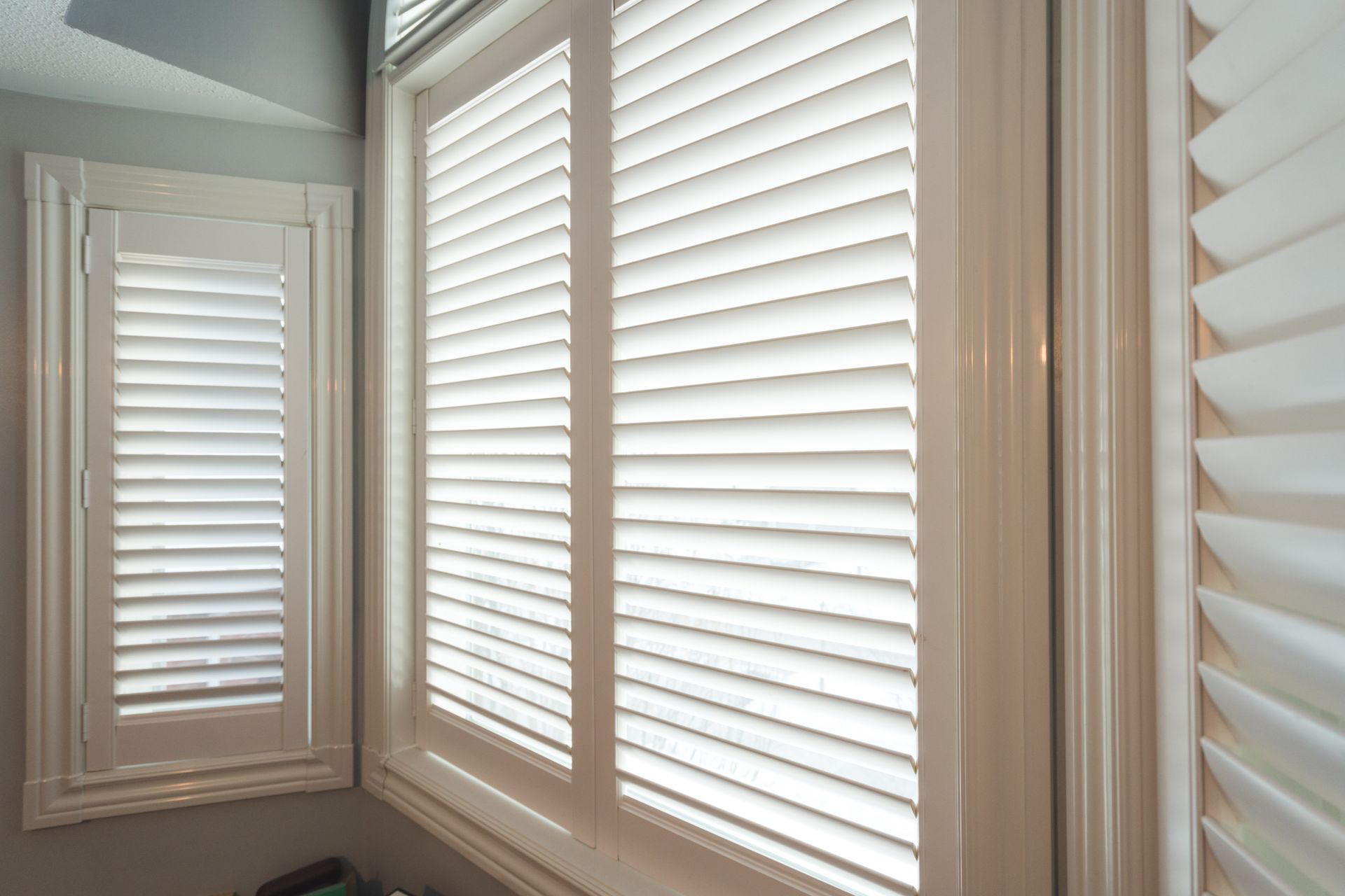 White wooden shutters covering a bright window, softly filtering natural light indoors.