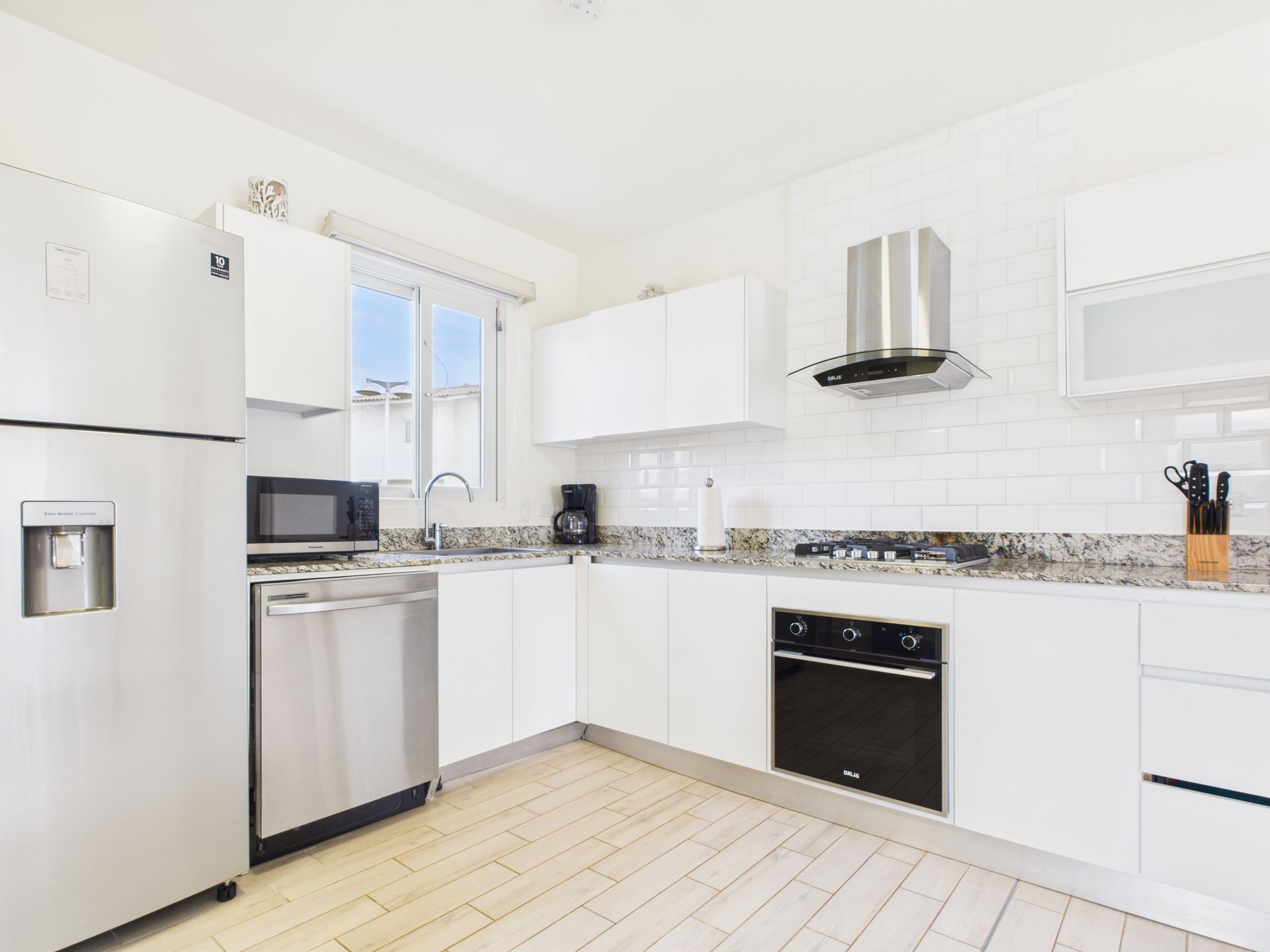 Modern white kitchen with stainless steel appliances and light wood floors.