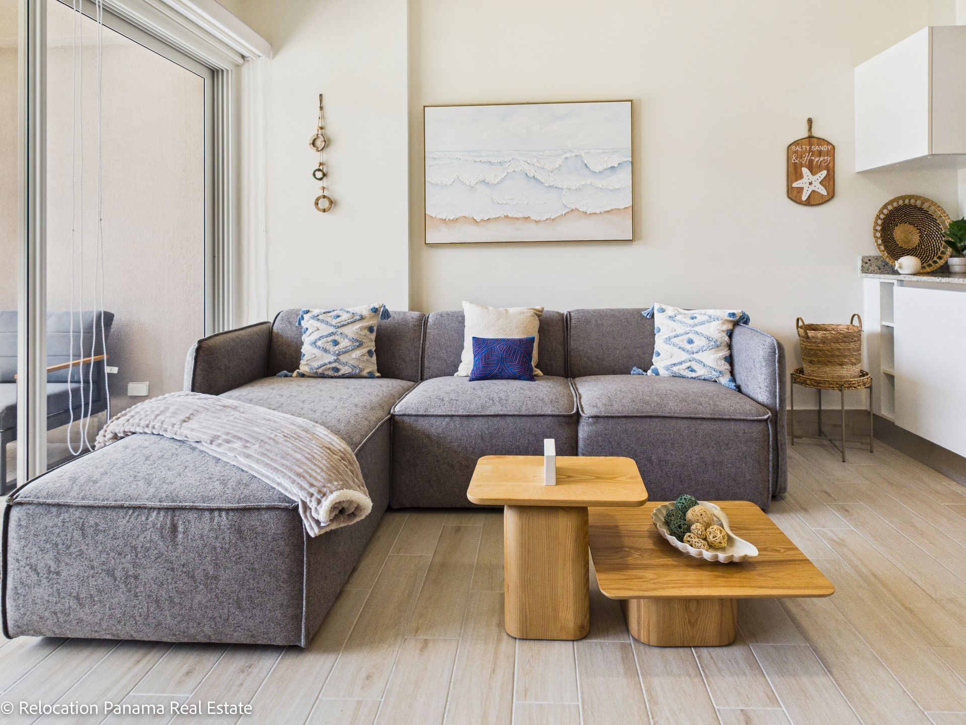 Un sofá modular gris con cojines estampados y una mesa de centro nido de madera en una sala de estar moderna de estilo costero.