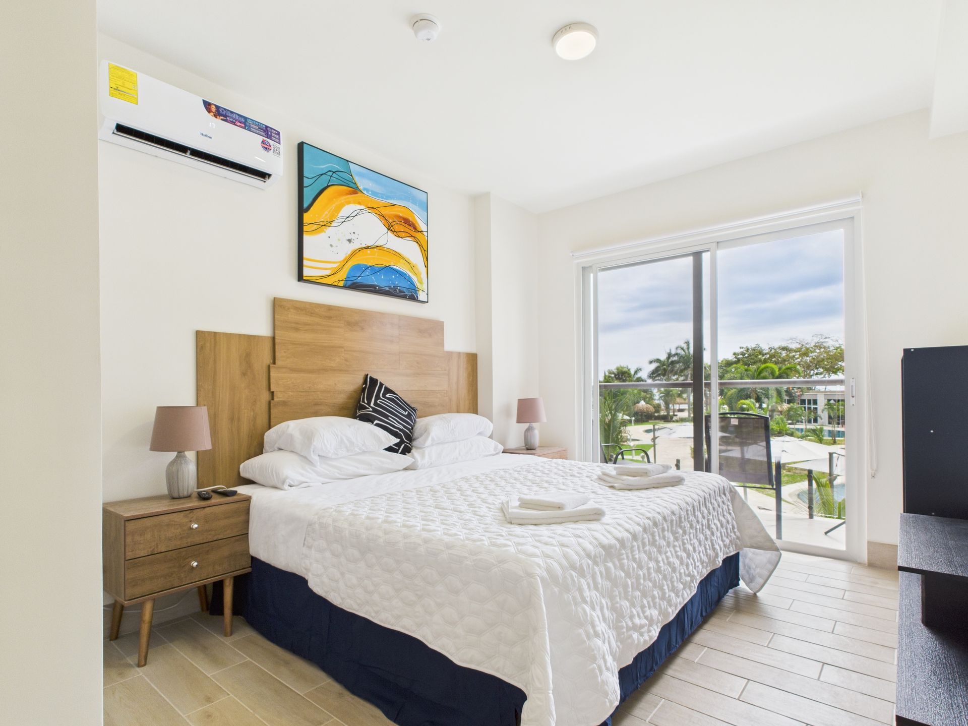 Bedroom with a bed, nightstands, artwork, and a sliding glass door to a balcony.