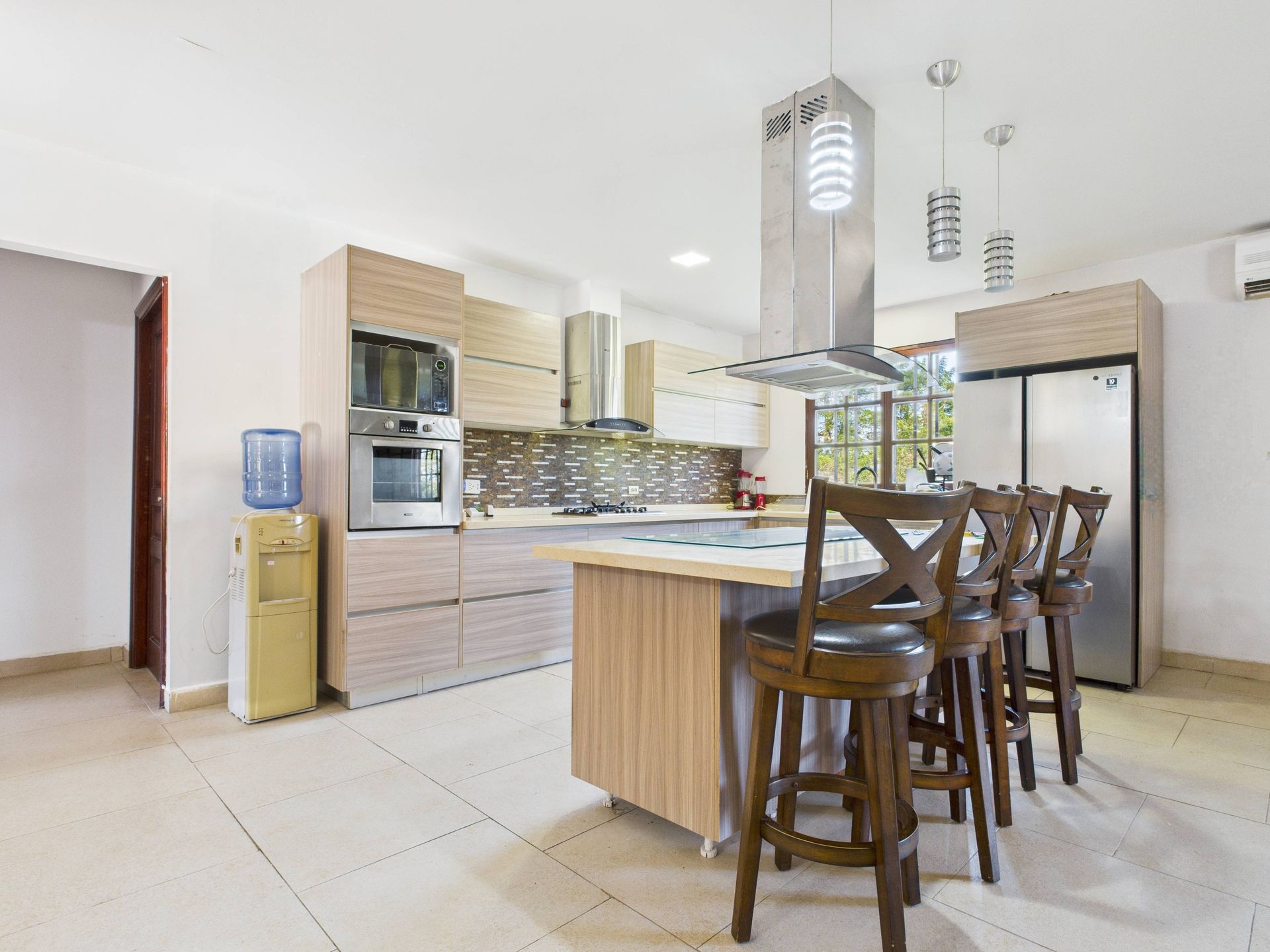 Cocina moderna con isla, gabinetes, electrodomésticos y taburetes de bar.