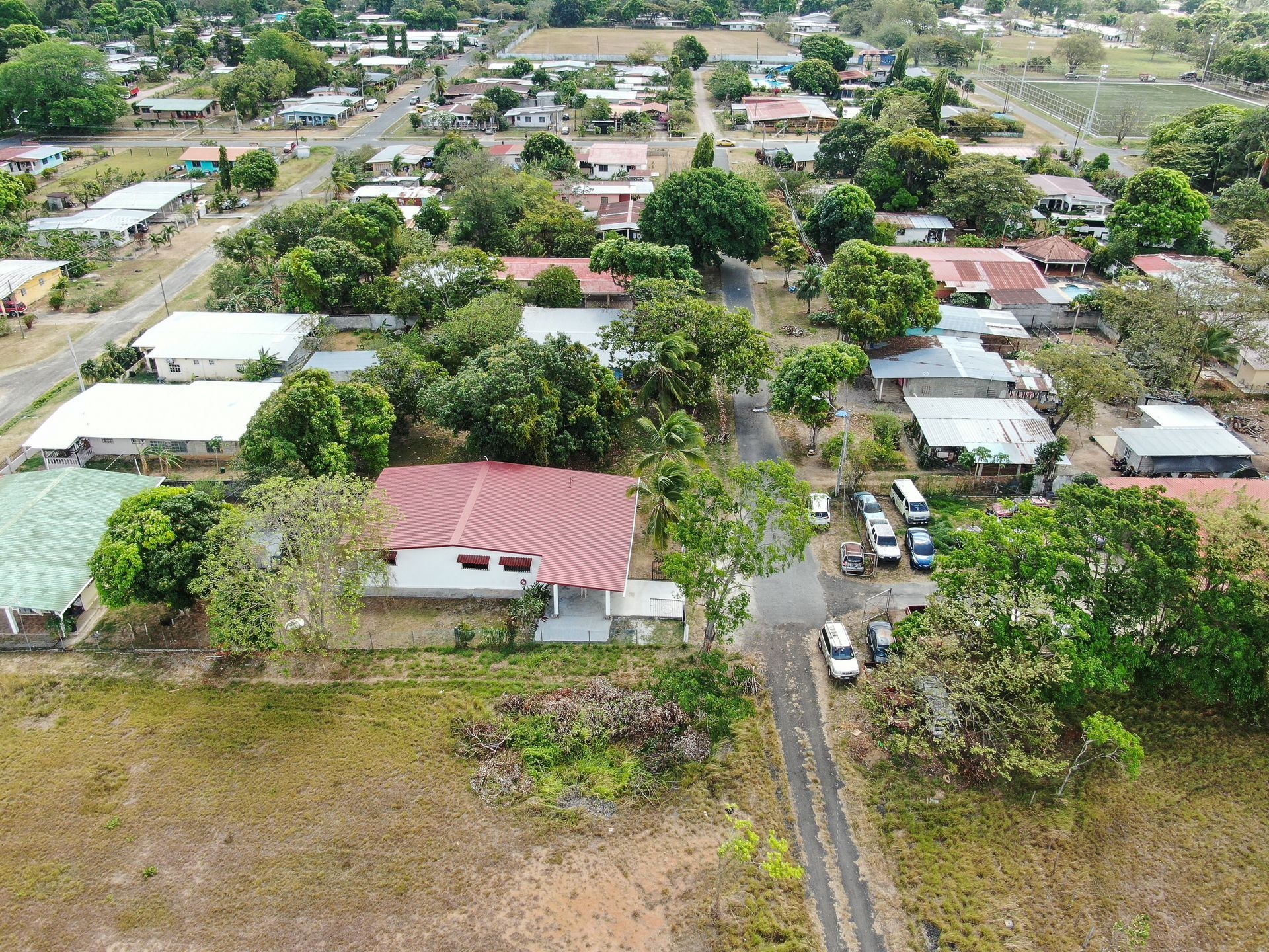 Vista aérea de un barrio residencial en anton cocle con una casa central que presenta un gran tejado rojo rodeado de árboles verdes.