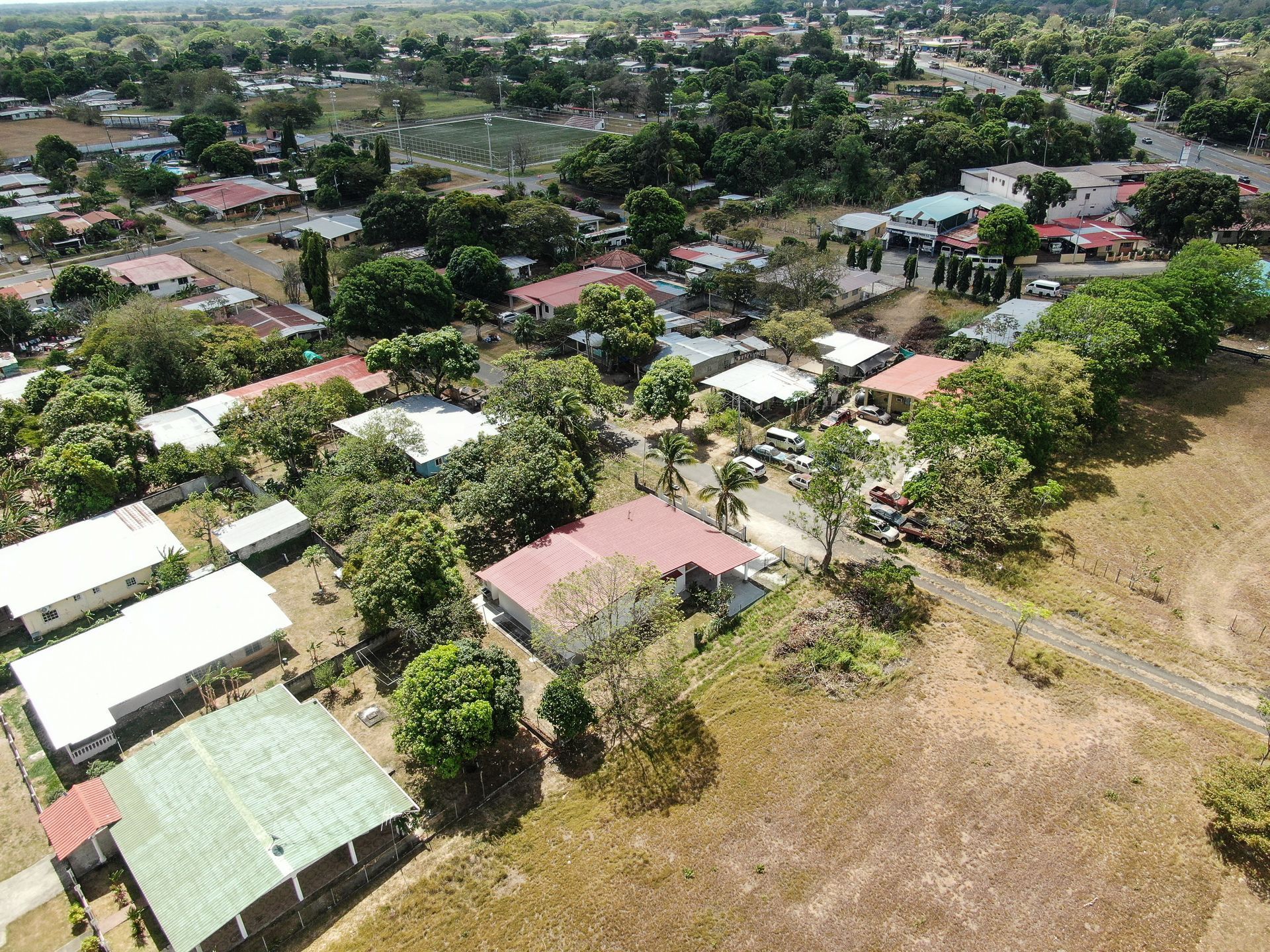 Vista aérea de un barrio residencial en anton cocle con una casa central que presenta un gran tejado rojo rodeado de árboles verdes.