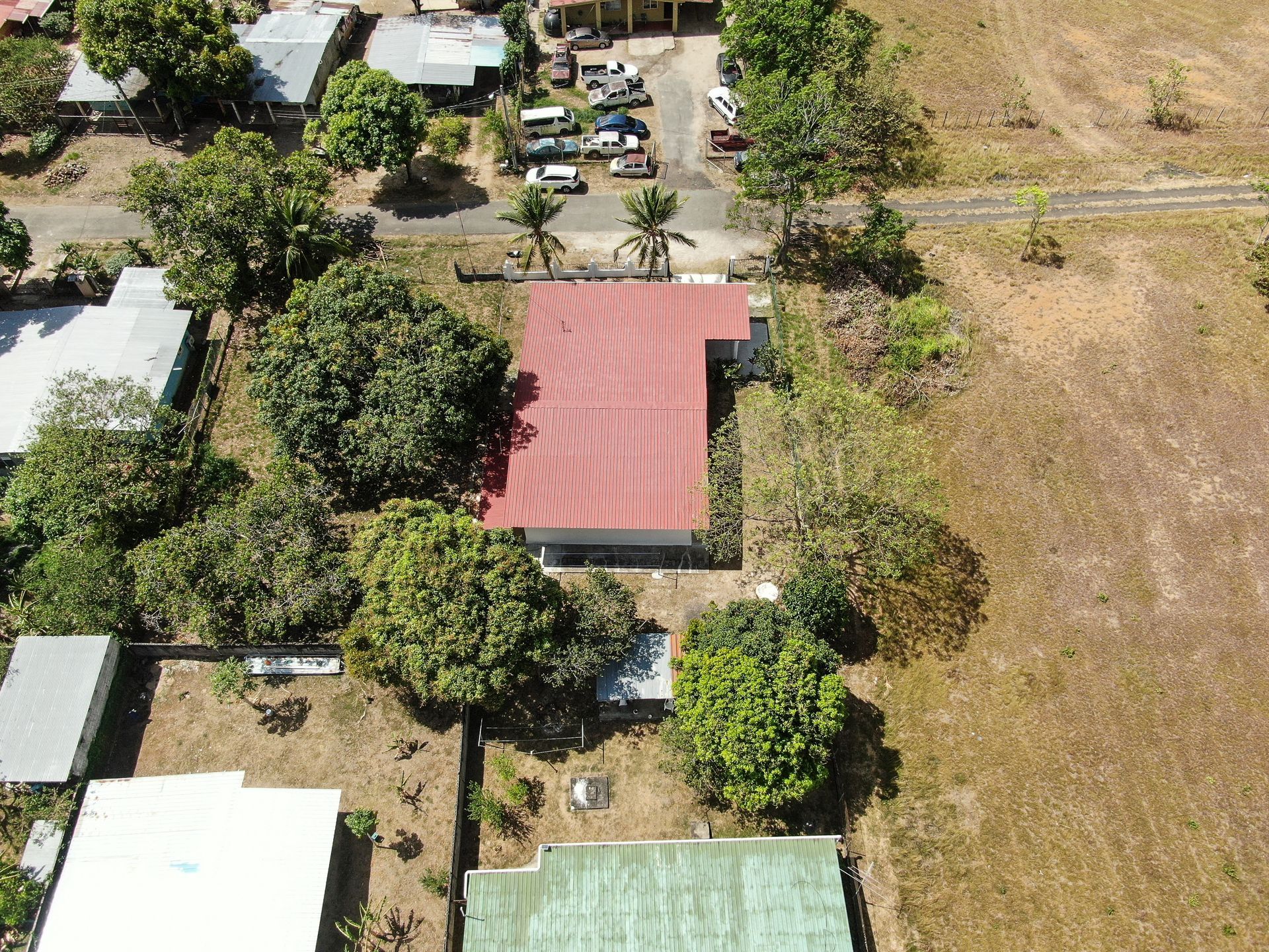 Vista aérea de un barrio residencial en anton cocle con una casa central que presenta un gran tejado rojo rodeado de árboles verdes.