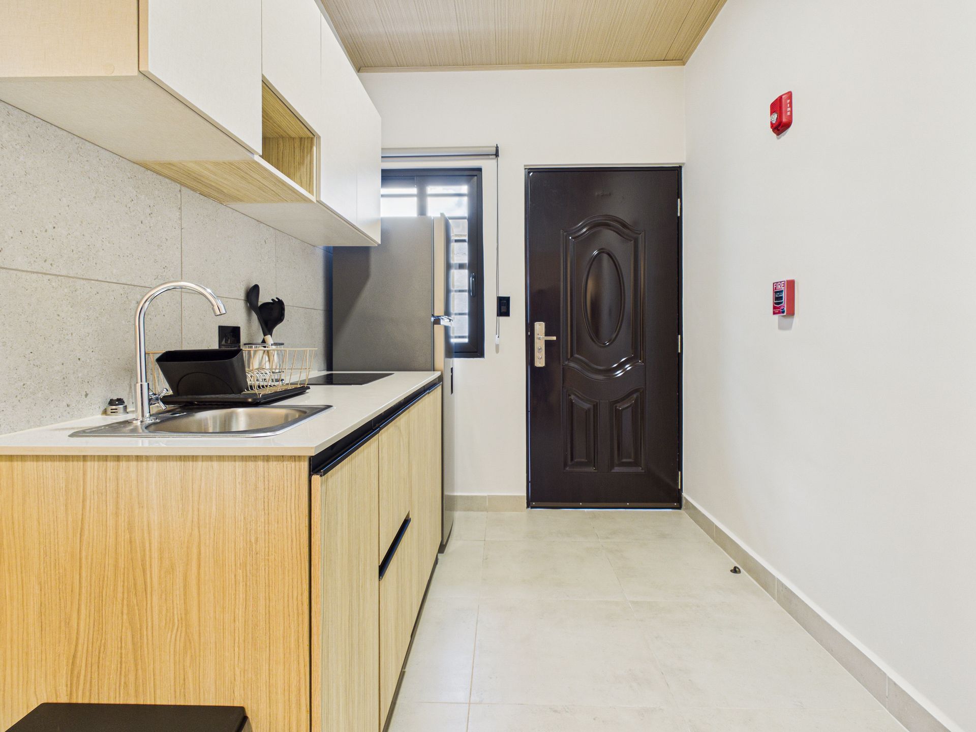 Una cocina compacta con armarios de madera clara, encimeras blancas, fregadero plateado, frigorífico de acero inoxidable y puerta de color marrón oscuro. en Bethania, fotografía inmobiliaria.