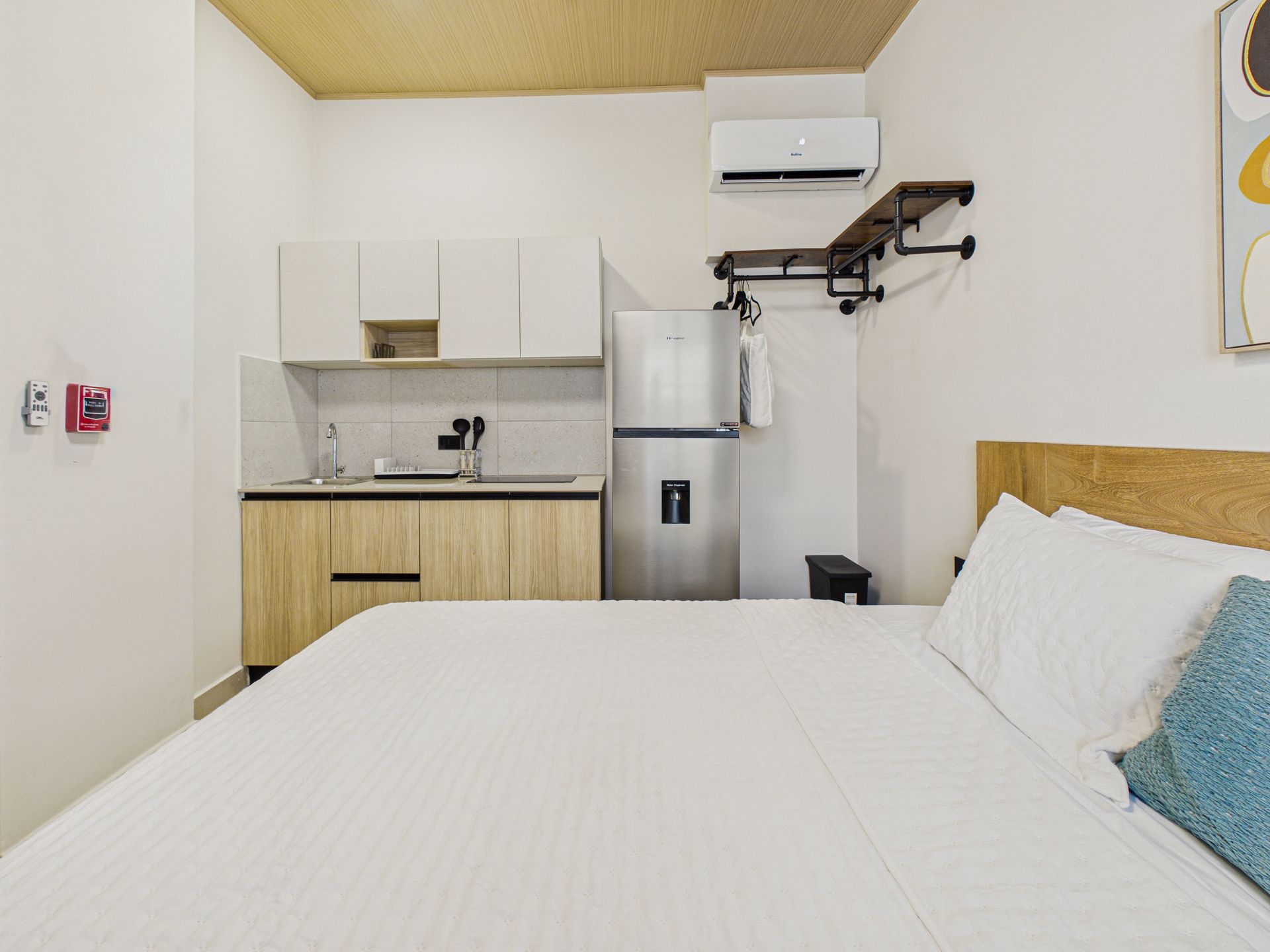 Una habitación de hotel con una cama grande en primer plano y una cocina pequeña con fregadero, armarios blancos y nevera. en Bethania, Ciudad de Panamá. Fotografía de real estate
