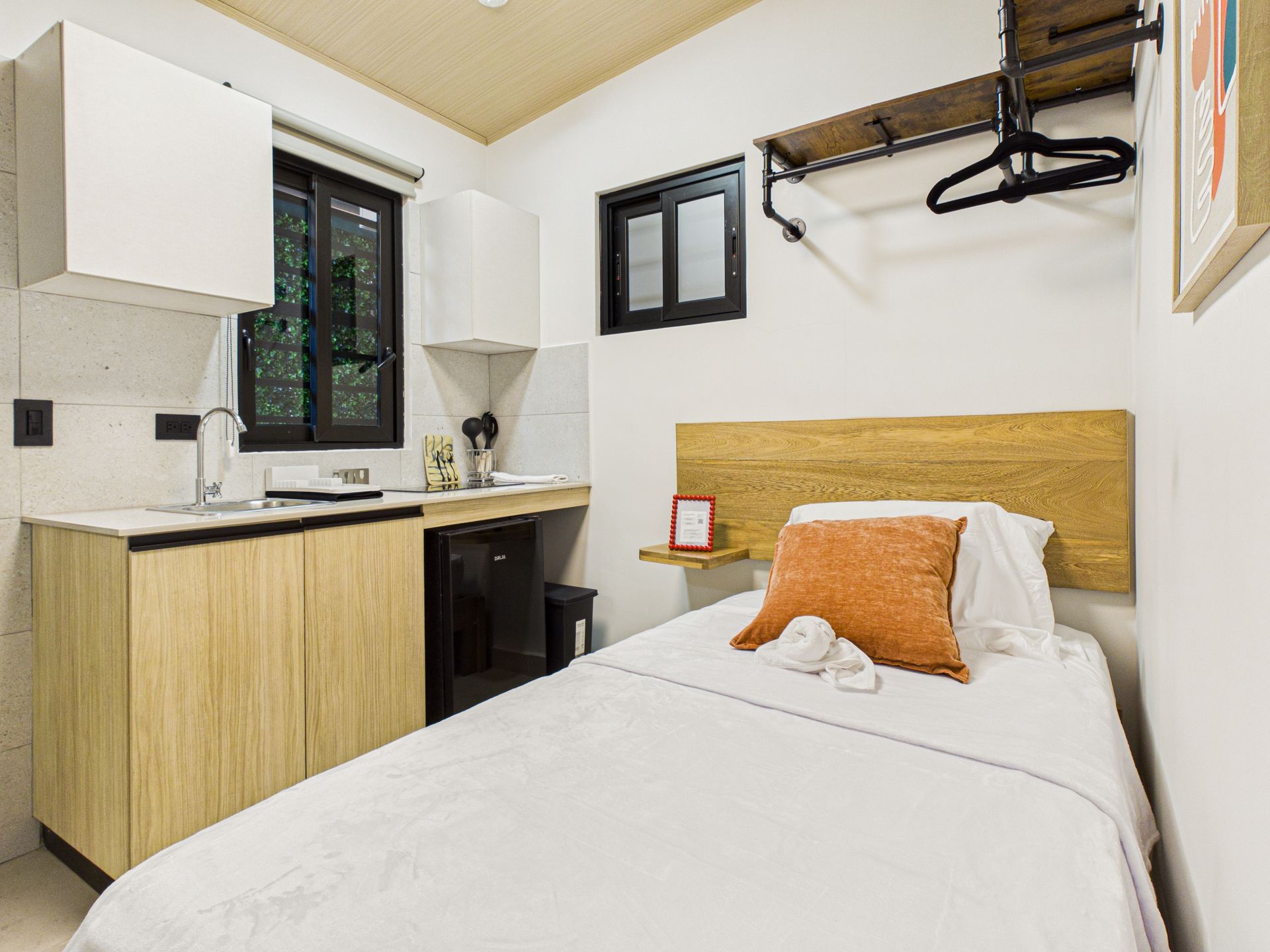 Un pequeño estudio con una cama individual, una cocina compacta con fregadero, armarios de madera y espacio de almacenamiento en la pared. en Bethania, Ciudad de Panamá. Fotografía de real estate