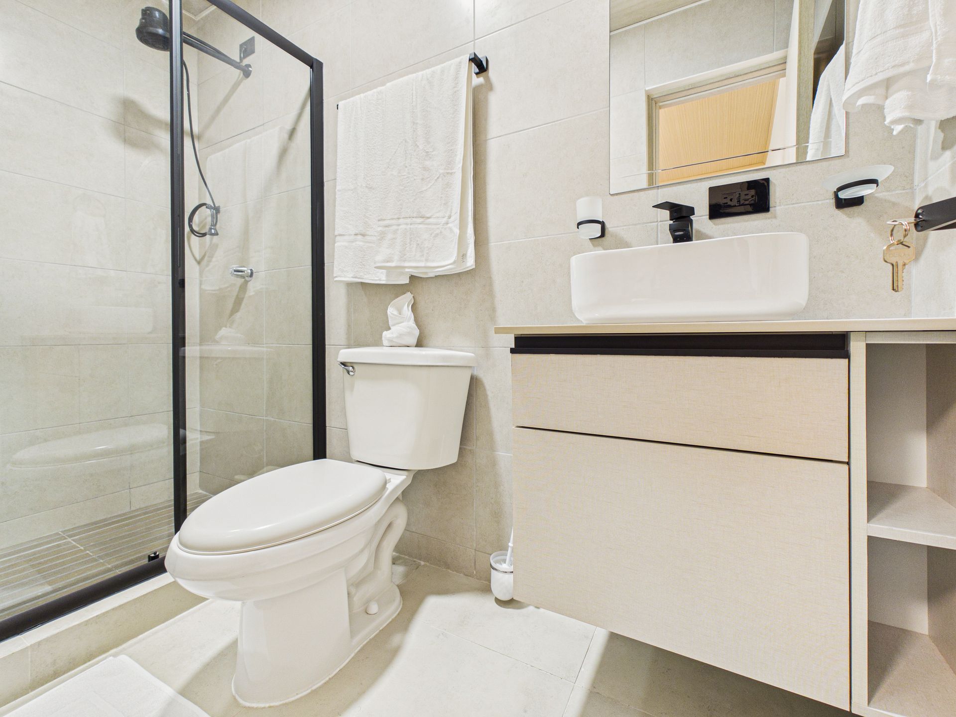 Baño moderno con cabina de ducha de cristal, inodoro blanco y tocador con lavabo rectangular y espejo.en Bethania, Ciudad de Panamá. Fotografía de real estate