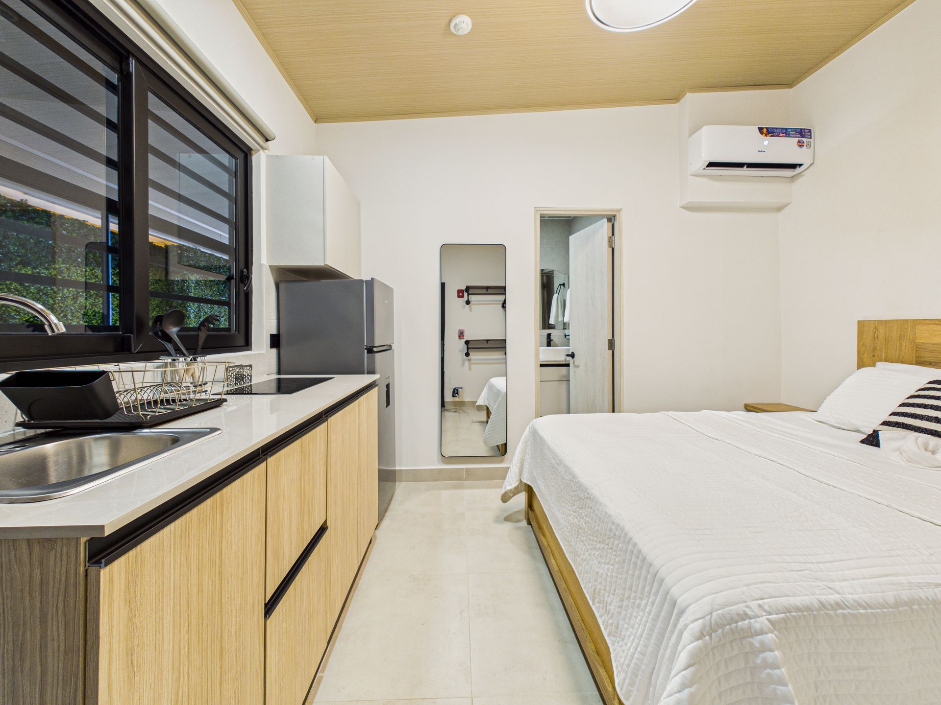 Un estudio con encimera de cocina de madera clara, nevera gris, cama blanca y aire acondicionado. en Bethania, Ciudad de Panamá. Fotografía de real estate